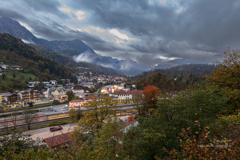 Ein Talkessel mit einer kleinen Stadt, starker Bewölkung und erstes künstliches Licht.