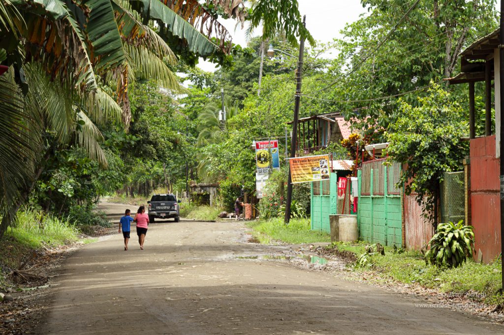 Eine Straße in Rio Blanco, es ist ein Sandweg mit zwei Kindern und bunten Häusern.